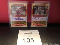 Both autographed cards from Robert Parrish and Michael Cooper side by side in protective cases against a red background, showing front of cards with signatures.