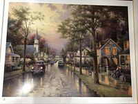 Full view of the Thomas Kinkade print showing the entire street scene with church steeple, houses, cars, and trees along a reflective wet road at dawn or dusk.