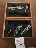 Full shot of the wooden box set showing 2 pliers multi-tools on top and 3 pocket knives organized in foam cutouts on bottom. Flashlight slot is empty.