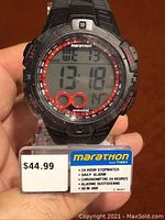 Front view of black Timex Marathon digital watch displaying time, date, day with features noted on display base including price tag of $44.99