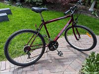 Side view of the maroon Schwinn bicycle showing the full frame, chain, pedals, rear derailleur, and knobby tires suitable for off-road use.