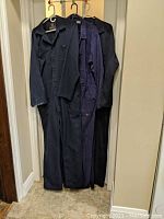 Three pairs of men's coveralls hanging on hangers showing different colors and styles.