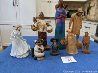 Photo showing the collection of all eight figurines arranged on a blue cloth, showcasing different sizes and materials including pottery, paper mache, corn leaves, and wood.