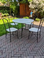 Table and 4 chairs set outdoors on brick patio with garden background