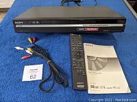 Front view of Sony DVD recorder with HDMI and 1080p upscaling label, AV cables, remote control, and manual on blue cloth.