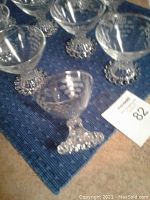 Close-up of multiple clear glass footed dessert cups with a cut grape pattern and hobnail footed bases arranged on a blue mat.