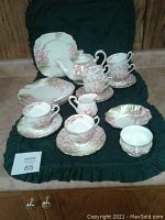 Full tea service arranged on green fabric background showing teapot, cups, saucers, plates, creamer, sugar bowl and mint dish