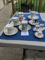 Full view of all 6 Royal Albert espresso cups and saucers arranged on blue cloth on outdoor table.