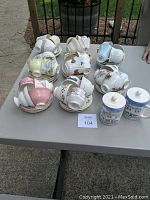 Eight sets of cups and saucers arranged on a table, showcasing various pastel and patterned designs with gold rims.