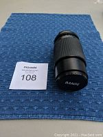 Black Image 80-200mm telephoto camera lens placed on a blue textured mat with front lens cap on, showing 'IMAGE' branding on the cap.