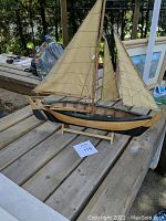Full side view of the fishing dory replica showing the sails, hull color, and wooden stand.