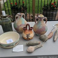 Eleven pieces of Southwest Native pottery including double-handled pitchers, Kokopelli wedding vase, painted bowl, and dried gourds on outdoor table.