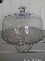 Footed cake plate with intricate cut glass pattern under clear plain dome