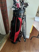 Full view of Wilson black and red leather golf bag standing upright in room, showing side and strap, with golf clubs inside