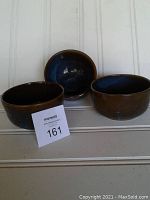 Three handmade ceramic bowls displayed side by side showing exterior brown glaze and interior blue glaze.