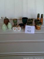 Full lot showing egg cups, pepper grinder, three sets of salt and pepper shakers, arranged on a shelf.