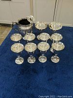 Group photo of 8 goblets, 2 champagne glasses, and 1 pitcher with reflective silver-tone finish displayed on blue fabric.