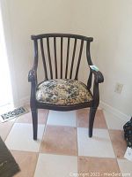 Front view of the wooden antique chair showing the floral upholstered seat and curved backrest with vertical slats.