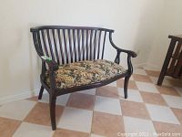 Antique wooden bench with floral upholstered seat viewed from a side angle showing detailed armrest and curved legs.