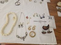 Full view of all costume jewelry items spread out on a white cloth, showing necklaces, earrings, brooches, and pins with MaxSold lot number visible.