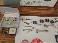 Top-down view of assorted men's accessories including tie clips, cufflinks, and pins laid out on a flat surface.