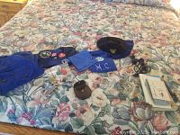 Wide layout showing blue fabric items, patches, booklets, and belts spread on a floral bedding.