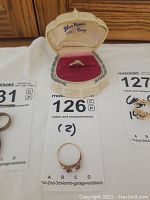 Blue River ring displayed in its original hinged cream and burgundy box alongside the pearl and red stone ring laid flat on tags