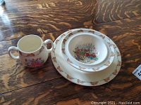 Front view of Bunnykins dishware set including two bowls stacked and two-handled cup showing bunny illustrations and border
