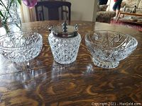 Three pieces on wooden table: two crystal bowls with detailed cut patterns and one diamond cut glass ice bucket with silver-colored lid.