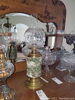 Antique painted brass oil lamp with floral motif, placed on wooden surface in front of carved wooden mirror.