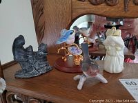 Shot of the wolf soapstone carving, porcelain bird figurines (blue and pink), and Belleek angel-shaped pitcher on a wooden surface with carved wood background.
