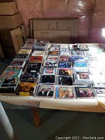 Table with a large selection of CD jewel cases arranged in rows and stacks, covers visible with various music genres shown.