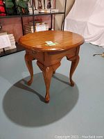 Front view of the oval wooden side table showing the top surface and front cabriole legs.