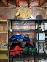 Wide shelf view showing wooden model sailboat on top shelf; middle shelf with blue fins, snorkeling masks and snorkels; bottom shelf holds red and green life jackets.