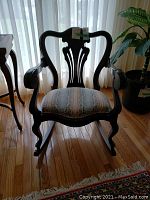 Front view of antique wooden rocking chair with upholstered seat and decorative backrest.