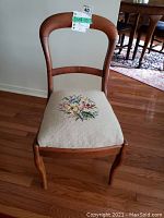 Front view of the antique wooden chair showing the embroidered floral seat and curved backrest