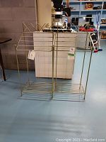 Full view of two gold-tone metal towel racks standing side by side on a floor, showing the entire racks including multiple horizontal bars and butterfly accents.