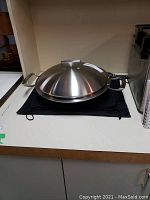 Stainless steel wok with lid placed on a black cloth with cabinet background
