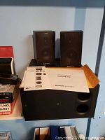 Photo of the full speaker system showing two satellite speakers, subwoofer, and manuals on top.