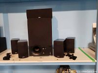 Full view of the Energy speaker system with one subwoofer in center, four satellite speakers on the sides, all black with fabric fronts, and mounting hardware included.