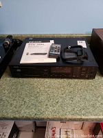 Front view of Denon stereo CD player on counter with remote and manual placed on top, showing model details and connectivity ports on the back.