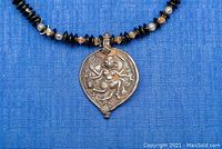 Close-up of silver pendant showing intricate Shiva engraving and surrounding gold and black beads of the necklace.
