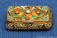 Angled view illustrating the raised detailed silver engraving on the sides and the enamel work on top