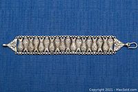 Top view of the full silver bracelet showing linked fish motifs and T-bar clasp on a blue fabric background.