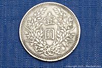 Front side of the silver Chinese coin showing laurel wreath and Chinese characters on blue background.