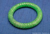 Green carved jade bangle with rope-like texture on blue fabric background, showing close-up details