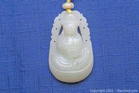 Close-up image of white jade pendant showing seated figure carving and cutout frame on blue fabric background.