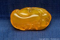 Front view of amber pendant carved with a dragon design under natural light on a dark cloth background.