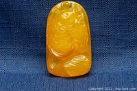 Front view of a carved goldfish amber pendant on blue textured fabric background