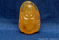 Front view showing detailed smiling Buddha carving in translucent orange amber pendant.
